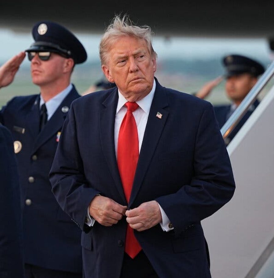 President Trump descending aircraft steps flanked by saluting airmen
